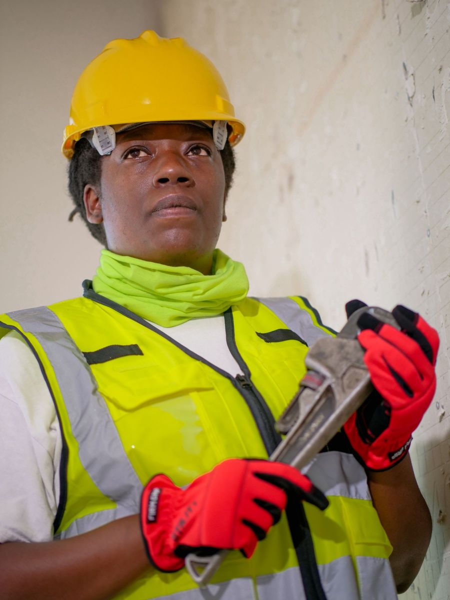 A tradeswoman in a hard hat holding a pipe wrench