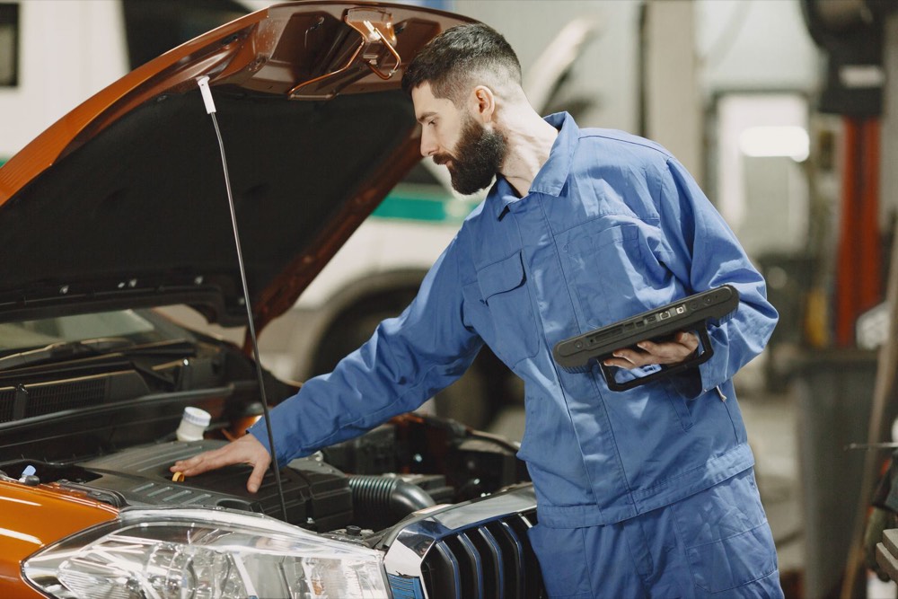 A mechanic in coveralls checking an engine under an open hood